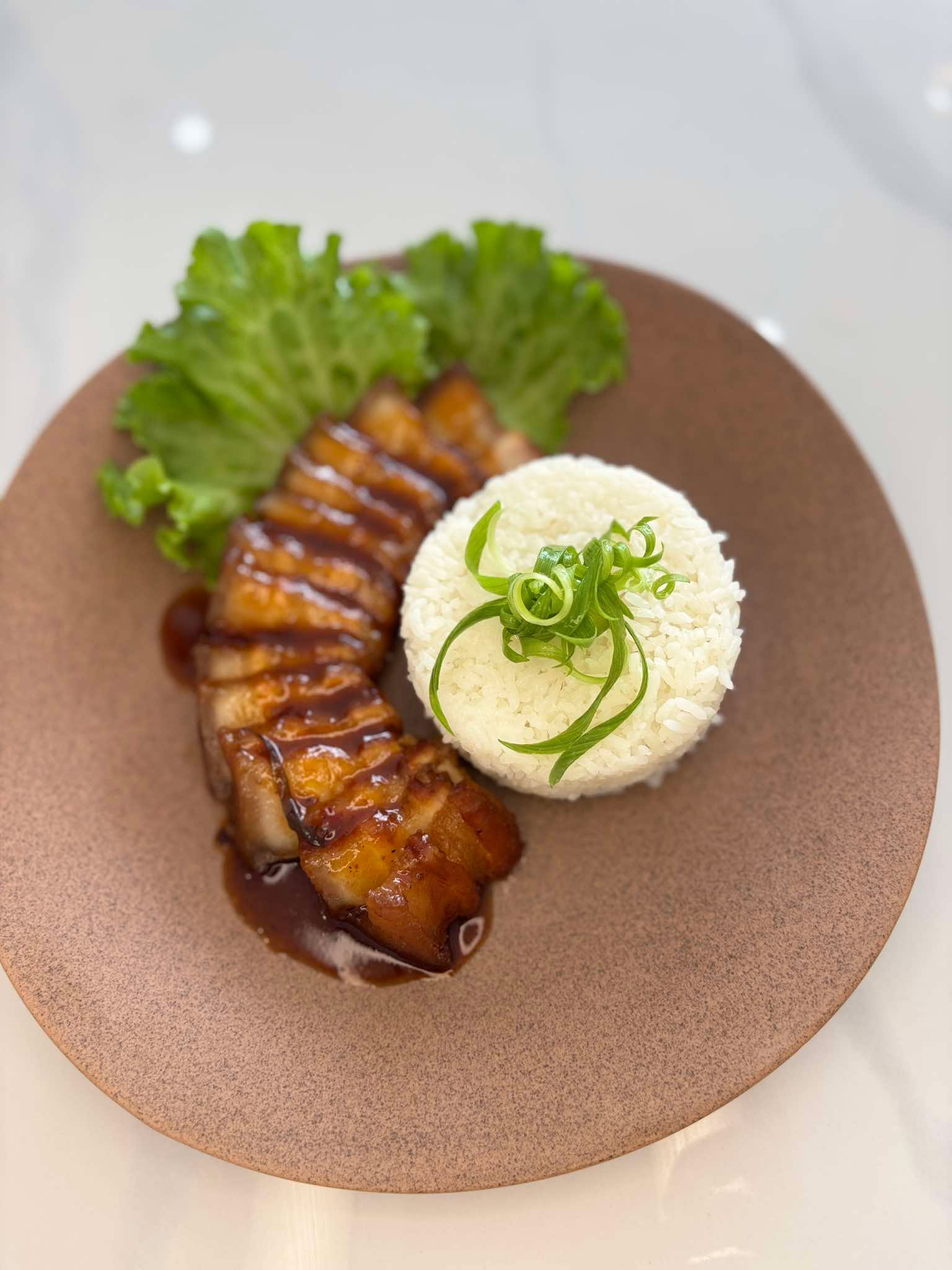 Glazed pork belly plated with steamed rice and lettuce